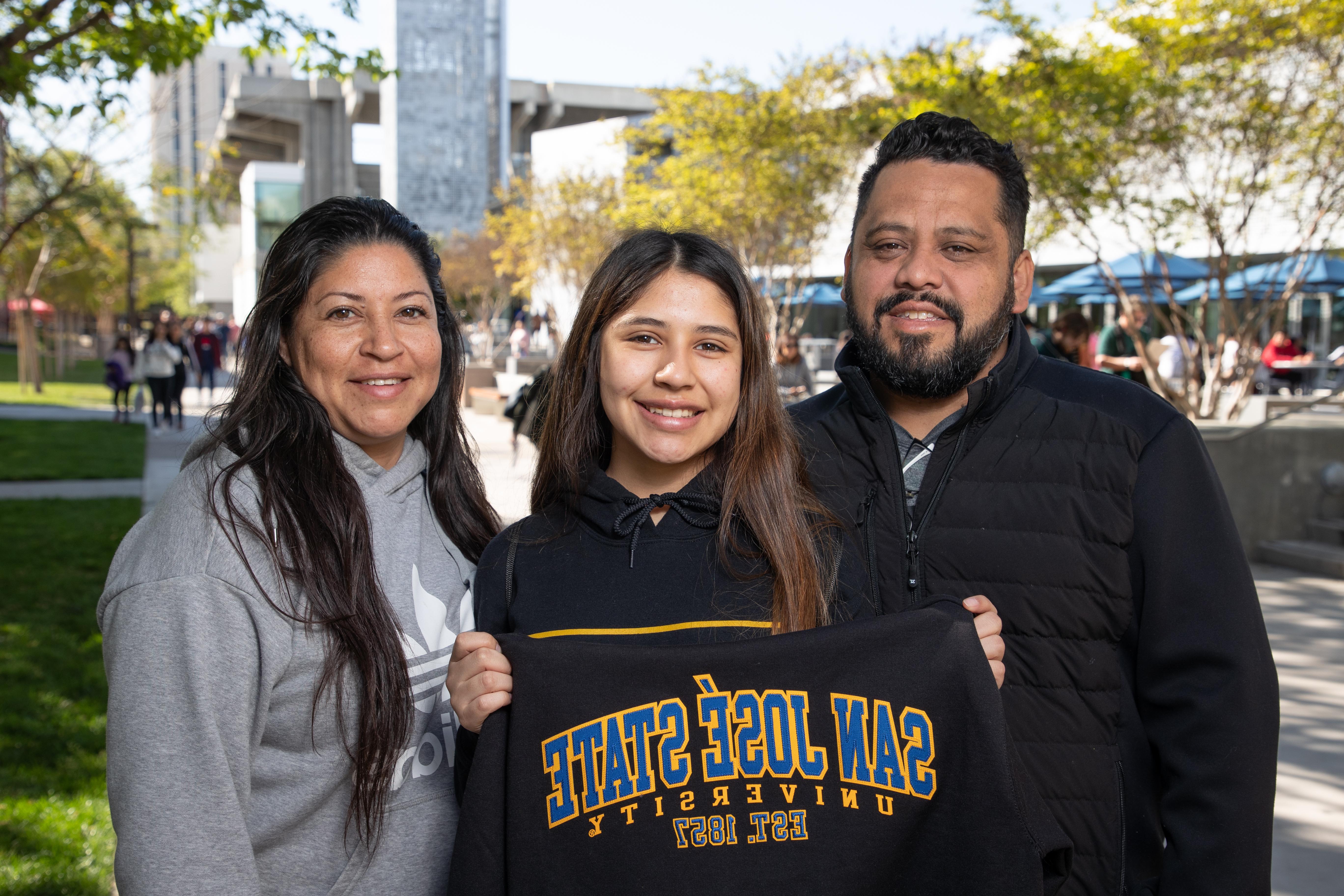 A student stands outside on campus with parents holding a 菠菜网lol正规平台 sweatshirt.